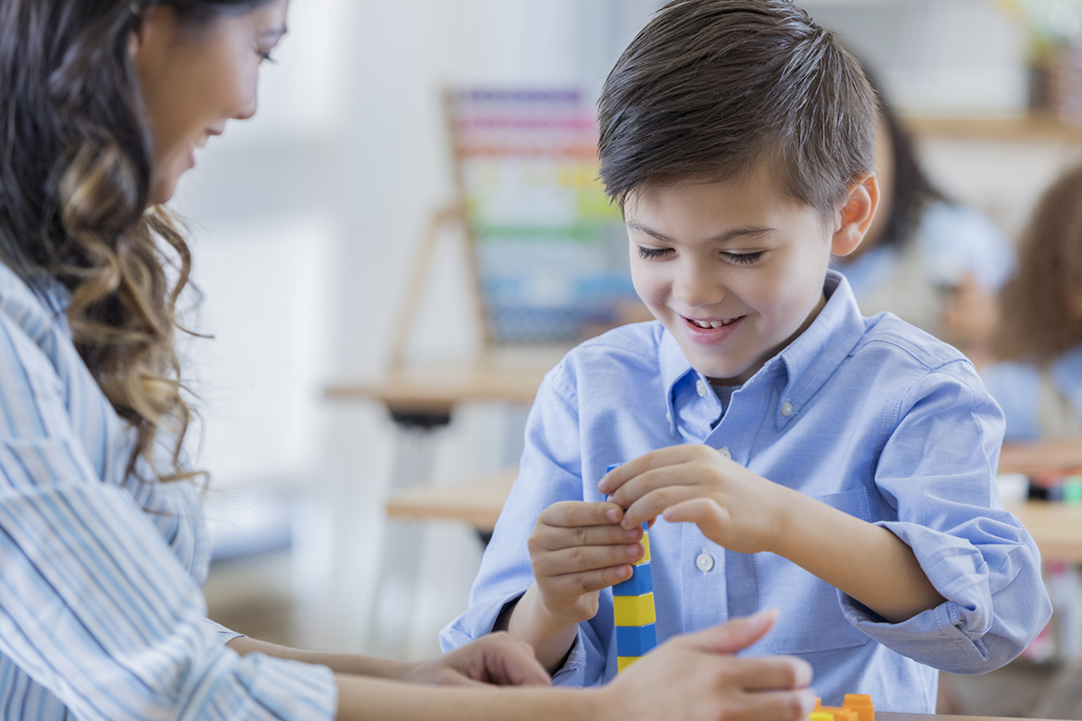 Primary school boy using hands-on counting blocks during maths class. His teacher is helping him.