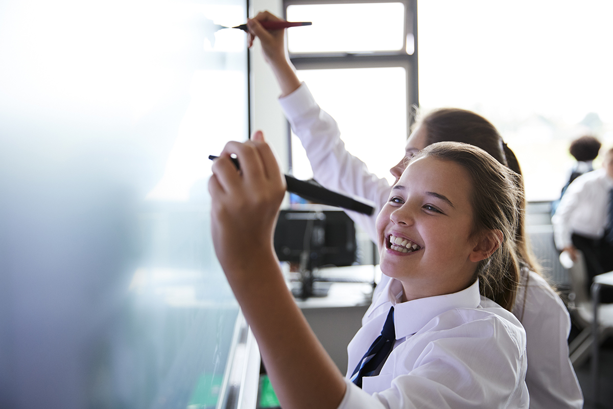 Female High School students wearing school uniform are sharing ideas and solutions using a whiteboard during a lesson.