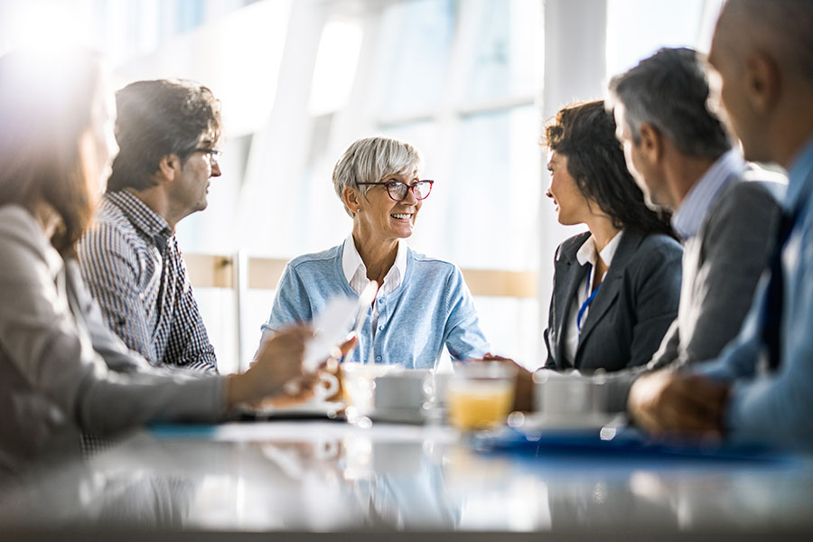 A business meeting around a table, six people, they have coffee, juice